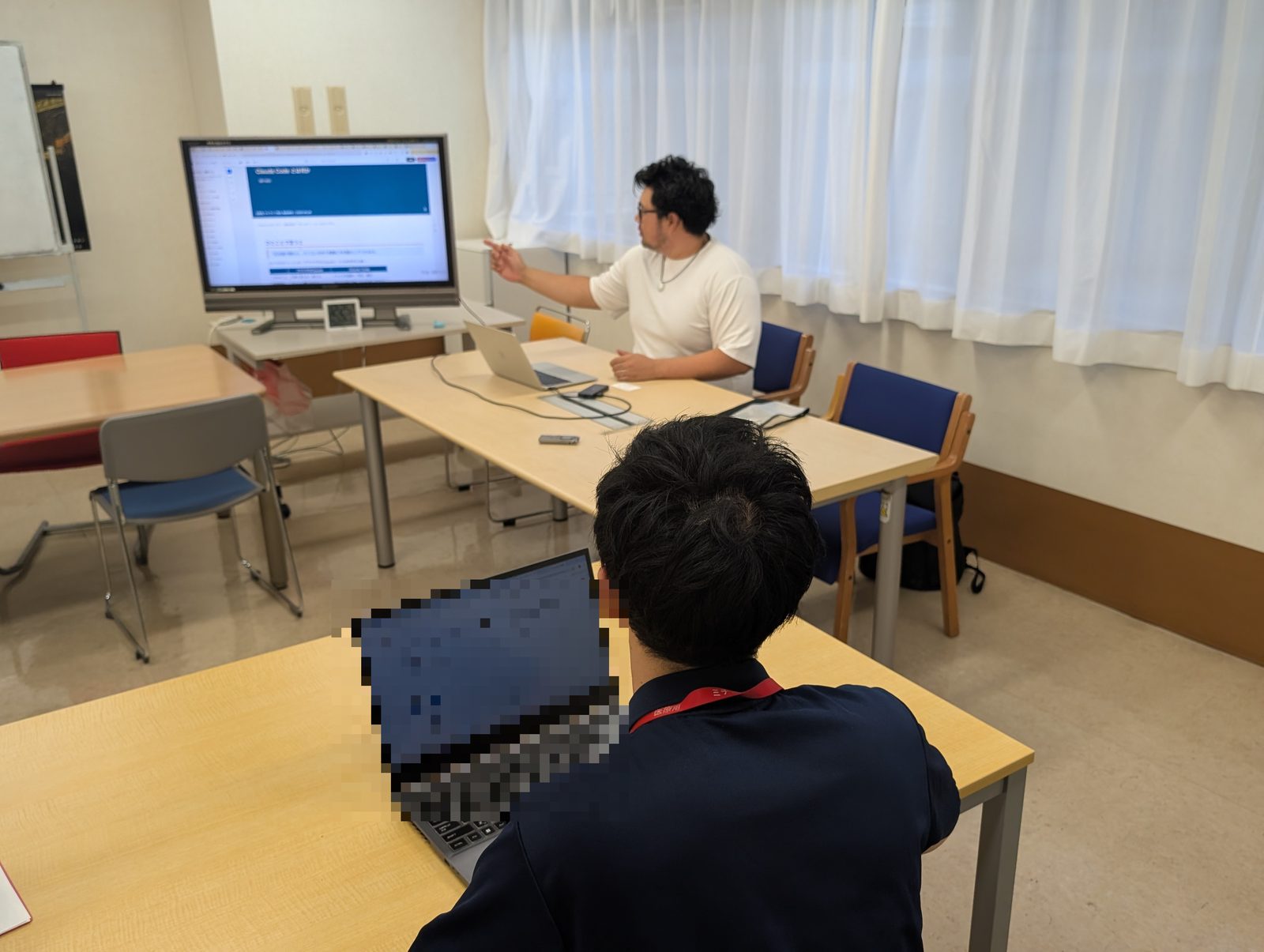 福祉施設で、合同会社サンの代表が職員に画面を示しながら、AIの具体的な使い方を説明している様子。